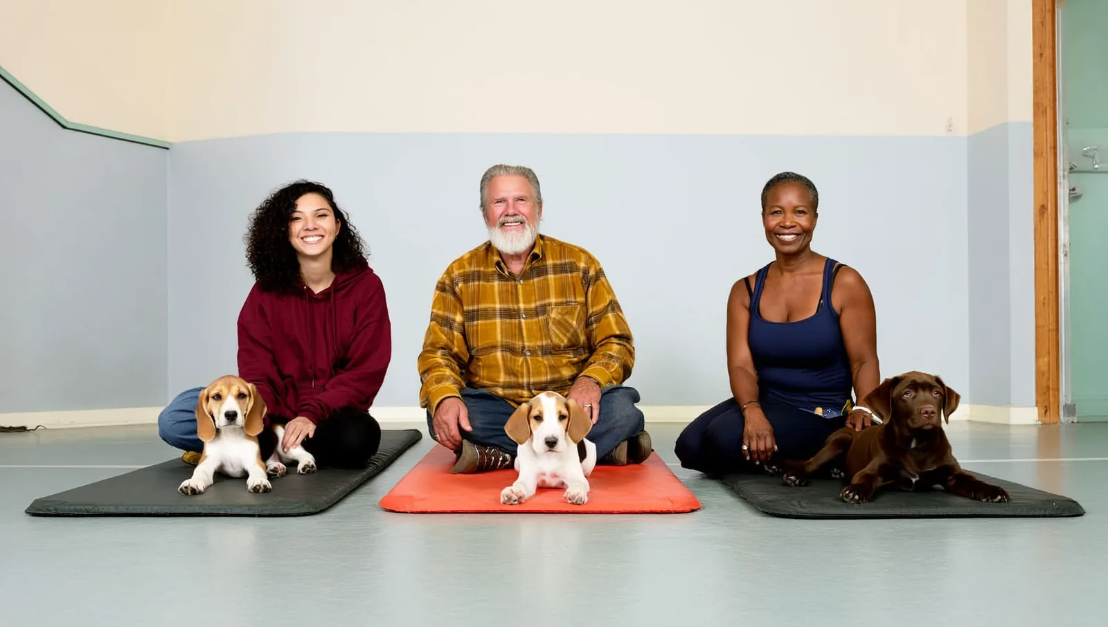 Three owners sitting on the floor of a puppy class, each beside their own puppy resting on a separate flat mat.